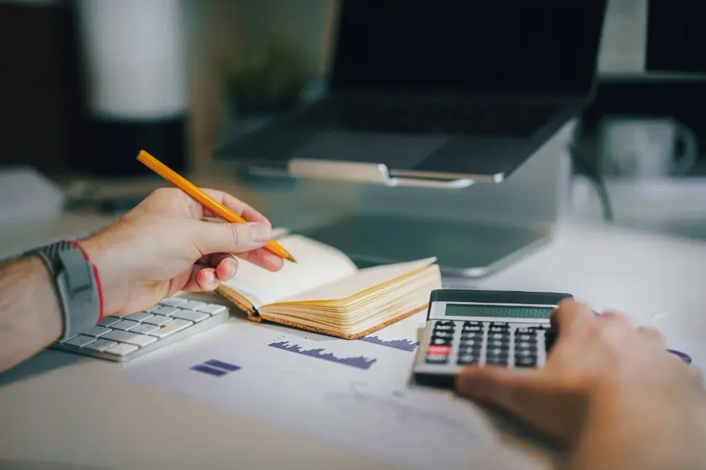 Hands using a calculator and pencil over financial charts and notes