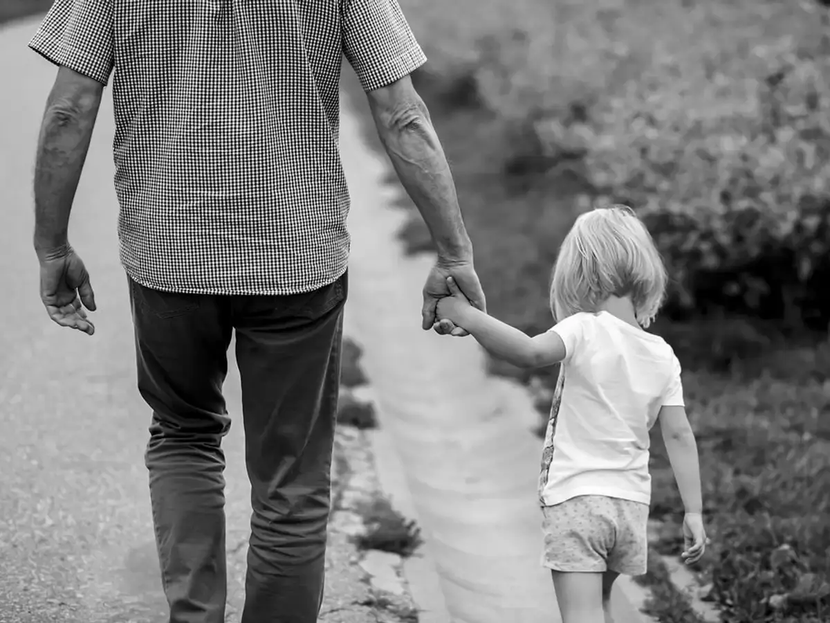 Grandfather and young grandchild walking hand in hand, seen from behind