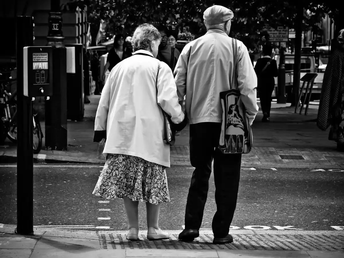 Older couple walking hand in hand along a street, seen from behind